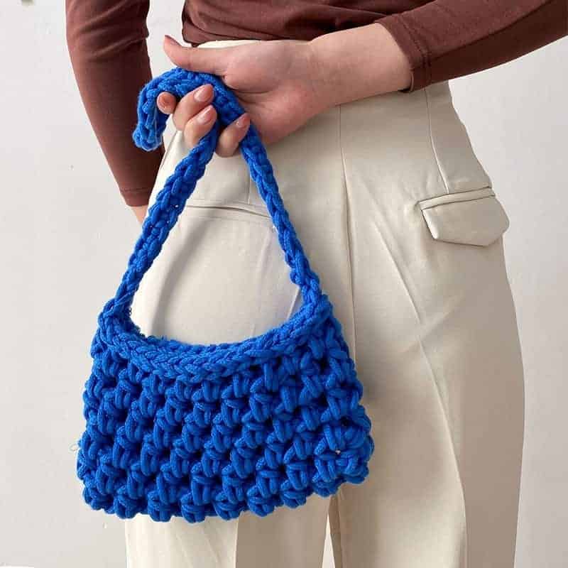 On voit une femme de dos habillée de manière très élégante avec un pantalon de costume Storlek ahute en lin Vit et un teee-shirt Brun à manches longues. Elle tient dans son dos un sac tissé en cordage Blå.