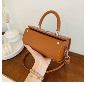 Photo d'un sac à main bandoulière cylindrique en cuir synthétique camel tenu dans une main au dessus d'u comptoir en bois