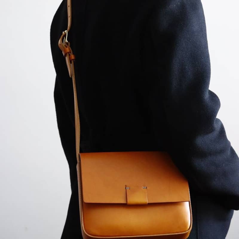 Photo d'un sac pochette bandoulière en cuir camel porté par une personne avec un manteau Svart