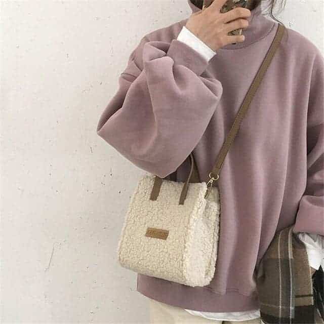 Petit sac à bandoulière en laine pour femme. Porté par une femme au sweat mauve.