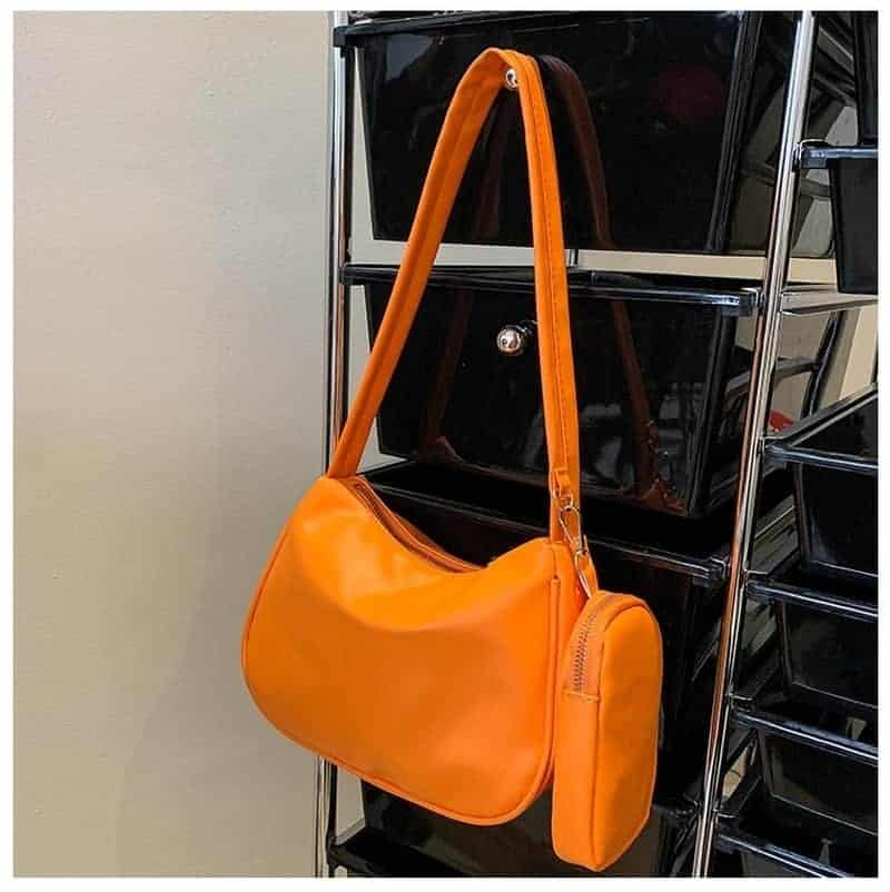 Sac bandoulière orange avec une petite pochette, accroché à une porte manteau en métal Svart