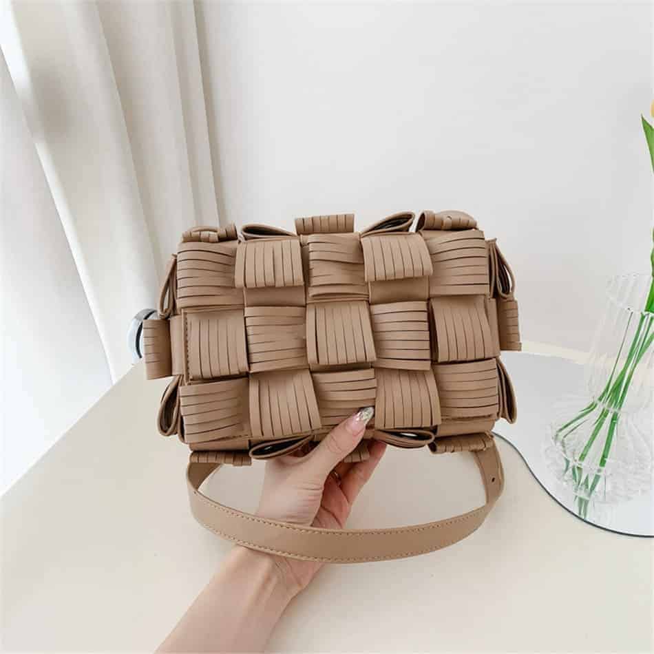 Photo d'un sac pochette à bandoulière en cuir synthétique texturé beige tenu dans une main au dessus du sol.