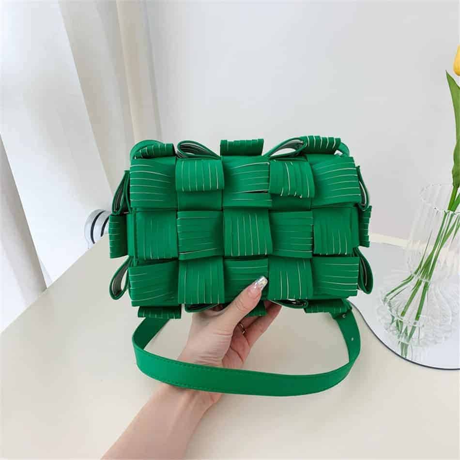 Photo d'un sac pochette à bandoulière en cuir synthétique texturé Grön tenu dans une main au dessus du sol.