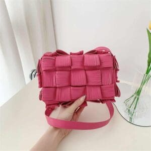 Photo d'un sac pochette à bandoulière en cuir synthétique texturé rose tenu dans une main au dessus du sol.