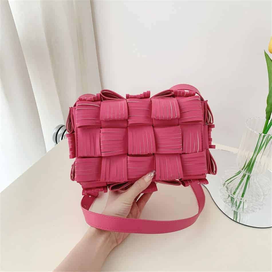 Photo d'un sac pochette à bandoulière en cuir synthétique texturé rose tenu dans une main au dessus du sol.