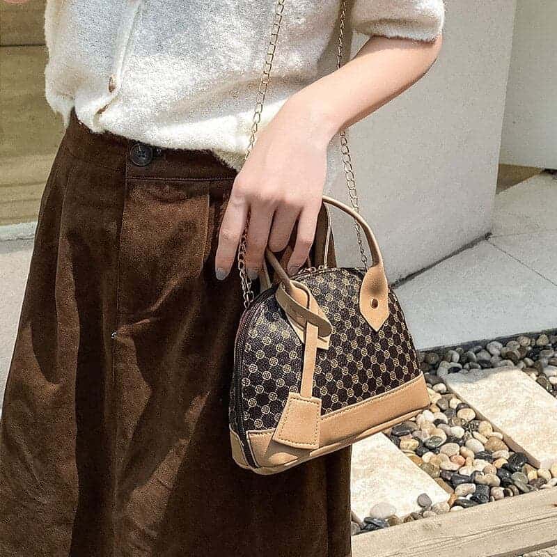 Petit sac bandoulière pour femme de luxe avec anse pour le tenir à la main. Contour Brun clair et forme arrondi et zippée sur toute la longueur.