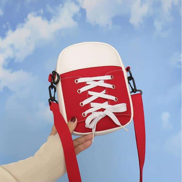 Sac en forme de converse Röd avec des lacets Vits tenu par une main avec un paysage de ciel nuageux derrière