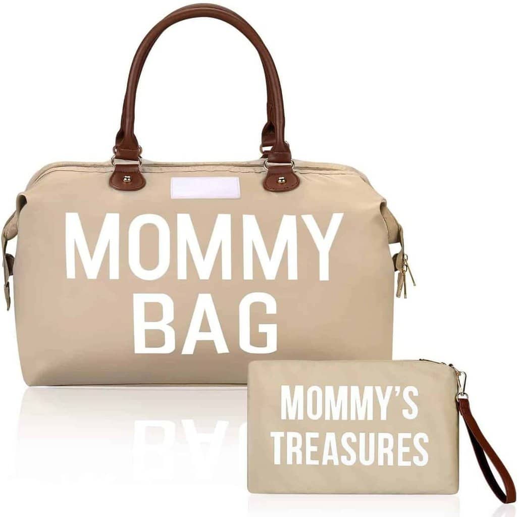 On voit un sac à langer avec une anse en simili cuir Brun. Il est beige avec une inscription MOMMY BAG. Il a une bandoulière pour garder les mains libres pour son bébé. Il y a une pochette assortie pour mettre dans le sac.