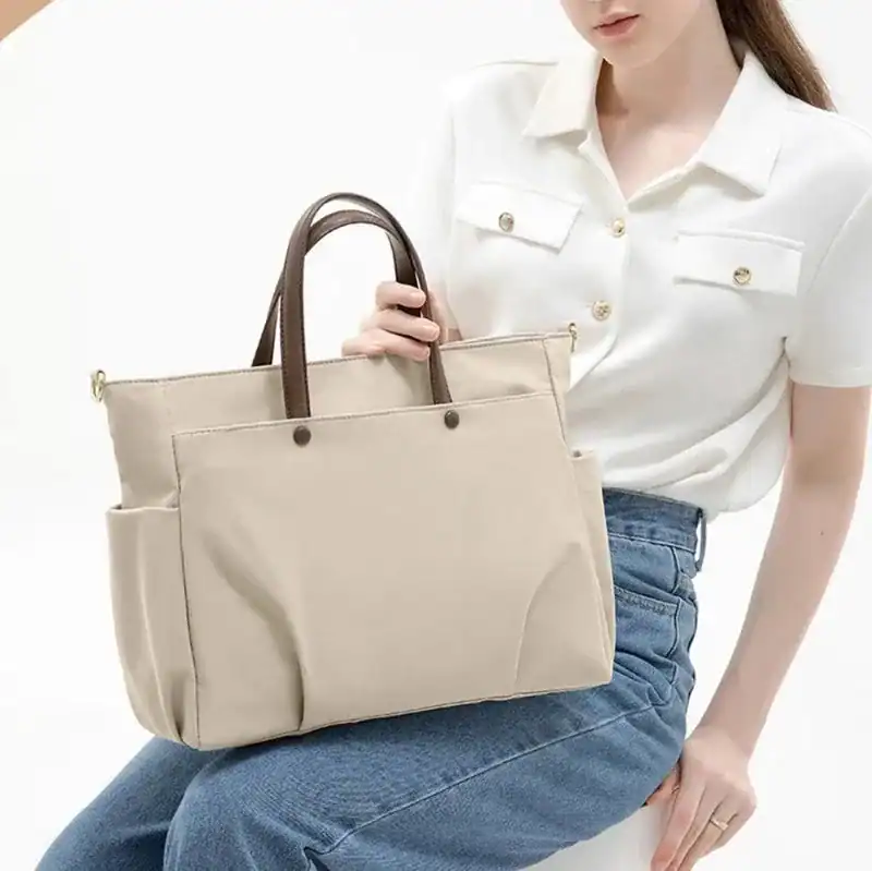 Beige datorväska med bruna handtag, passande för jobb och skola.