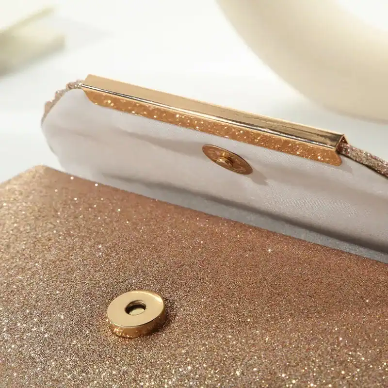 Beige glittrig clutch med guld detaljer och knapp.