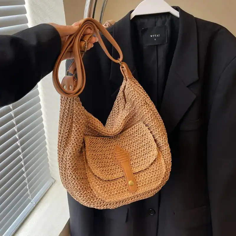 Beige halvmånsväska i rörvävt material med läderrem och plåtstängsel.