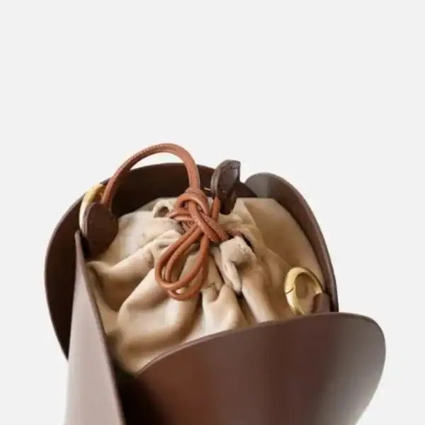 Beige hinkväska med hjärthängen i brunt läder, detalj på dragkedja och guldtonad ring.