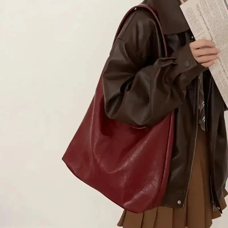 Beige hoboväska i röd läderliknande material, bärt av person i mörk jacka.