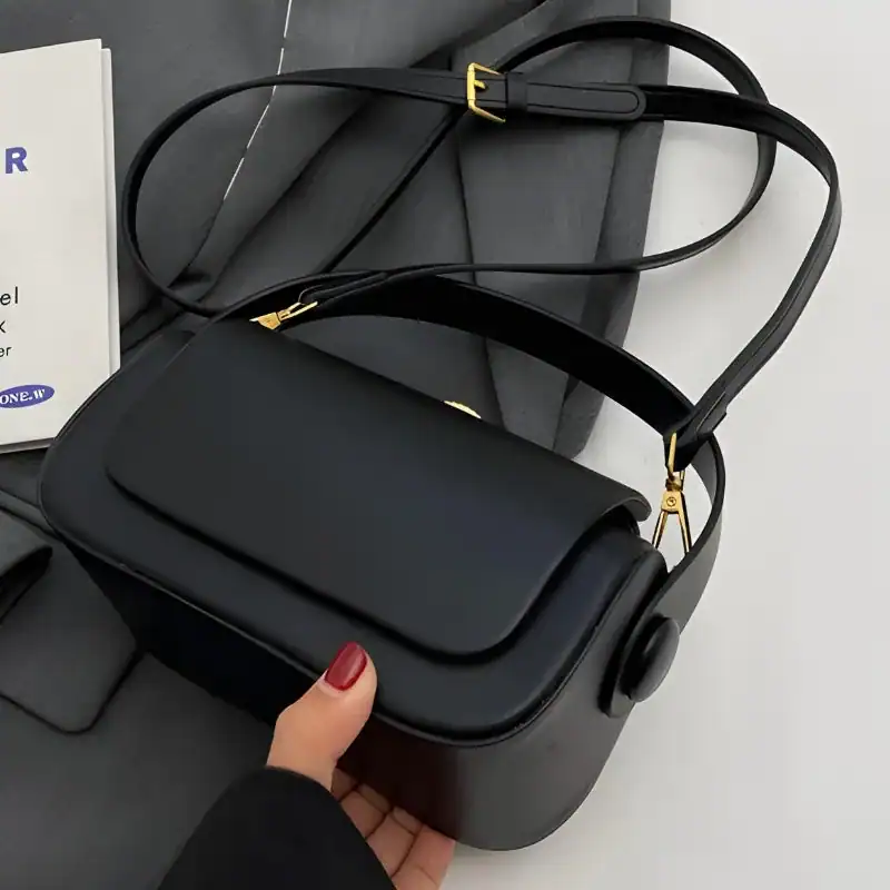 Svart liten crossbody axelväska med guldaccent och justerbar axelrem.