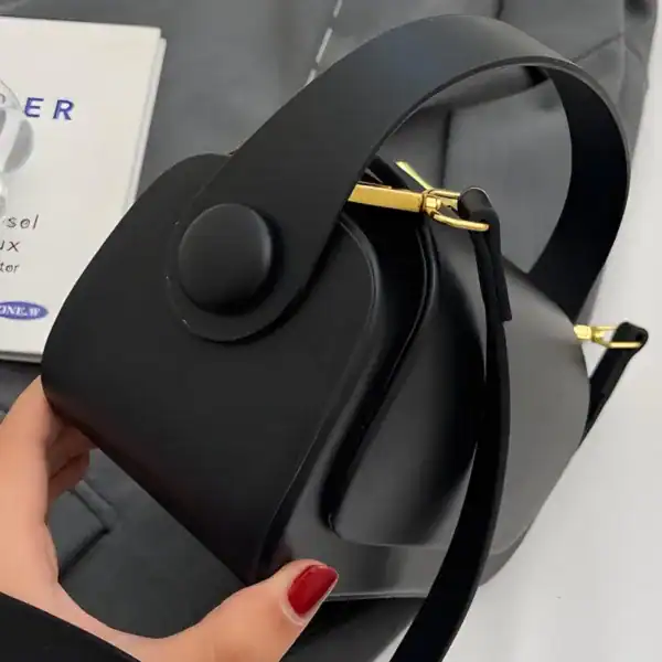 Svart liten crossbody axelväska med guldaccent och rund knapp.