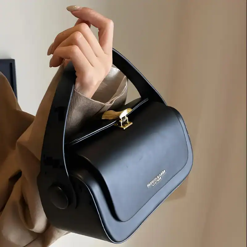Svart liten crossbody axelväska med guldaktig snabbklick och handtag.