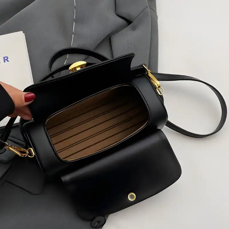 Svart liten crossbody axelväska med guldaccent och öppen inre.
