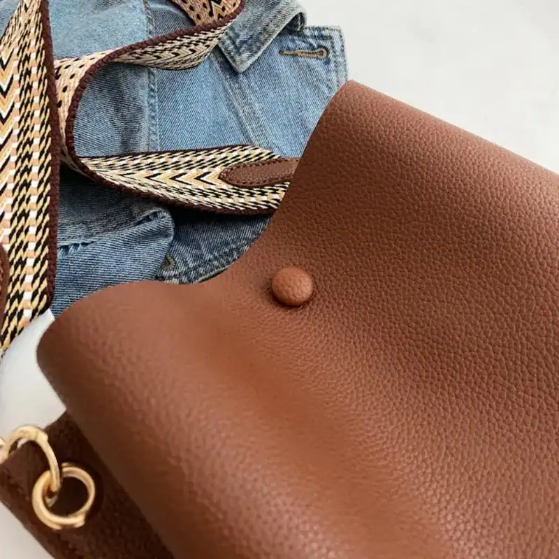 Beige liten hinkväska med mönstrad axelrem och jeans.