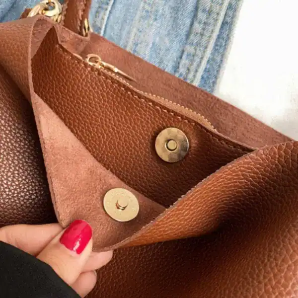 Beige liten hinkväska med guldtonade knappar och texturerat läder.