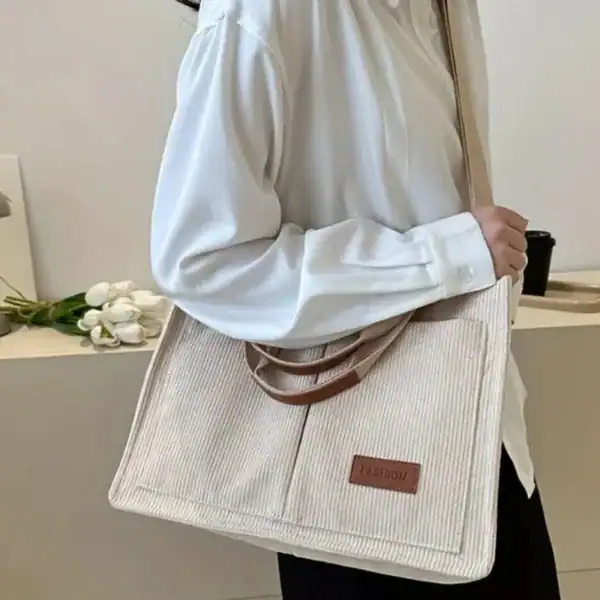 Beige manchesterväska med brunt läderhandtag och 'FASHION'-etikett.