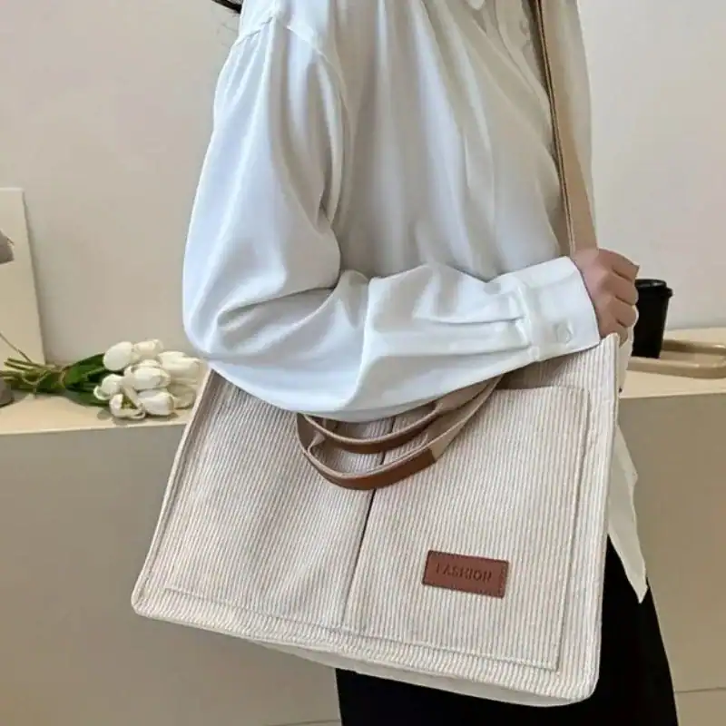 Beige manchesterväska med brunt läderhandtag och 'FASHION'-etikett.