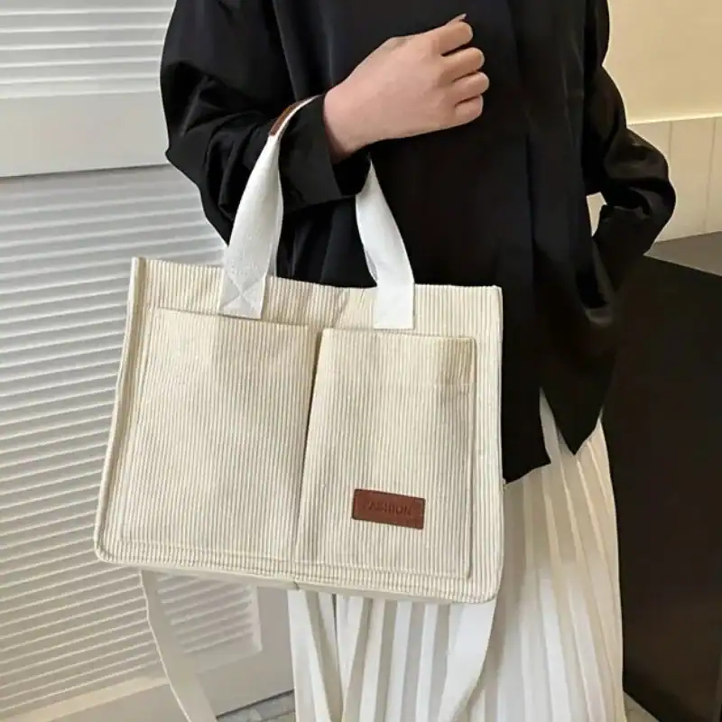 Beige manchesterväska med vitt handtag och brunt etikett.