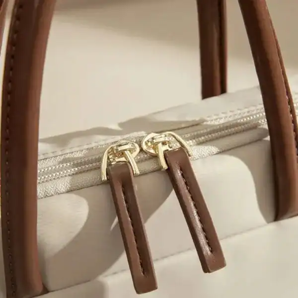 Beige nylon datorväska med bruna handtag och guldaktiga dragkedja.