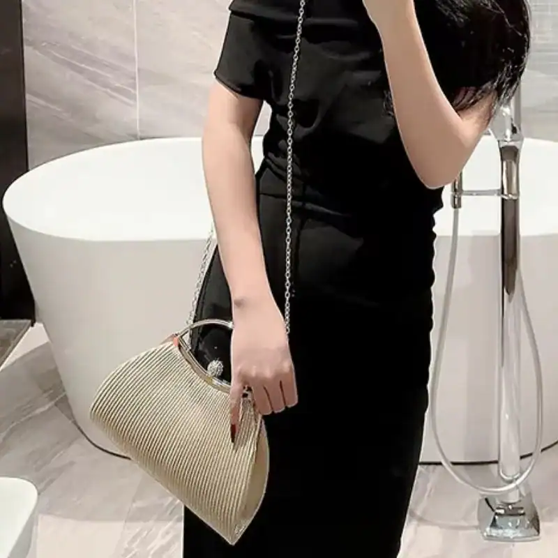 Beige plisserad clutch med kedjehandtag och metallringar.
