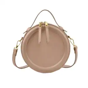Beige rund väska med axelrem och guldtonade detaljer.