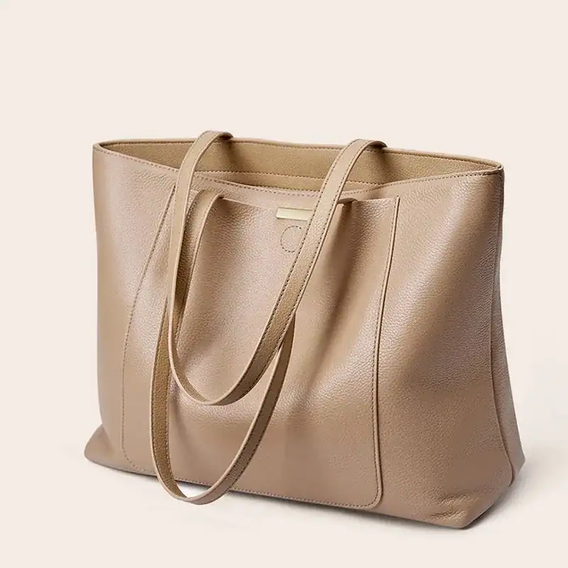 Beige shoppingväska i läder med långa handtag och minimalistisk design.