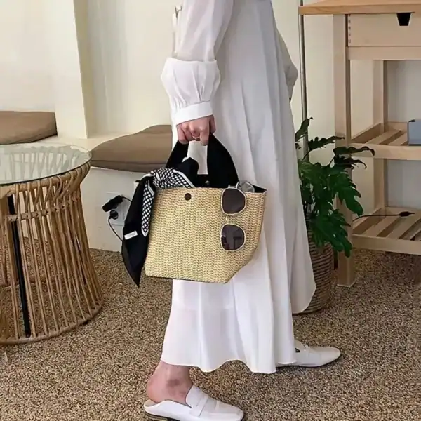 Beige stråväska med svarta handtag, fylld med solglasögon och halsduk.
