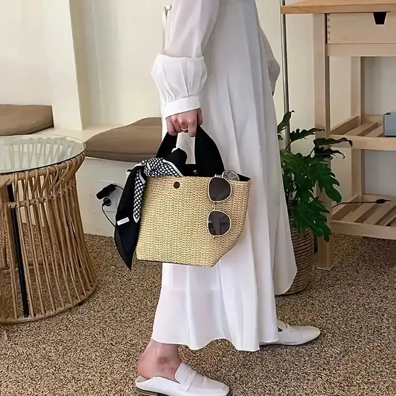 Beige stråväska med svarta handtag, fylld med solglasögon och halsduk.