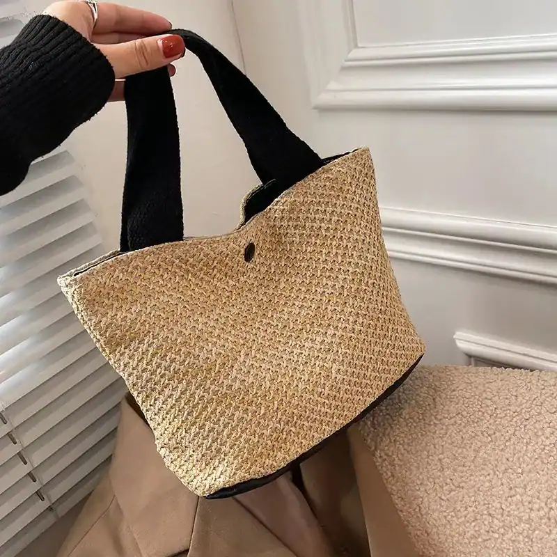 Beige stråväska med svarta handtag och elegant design.