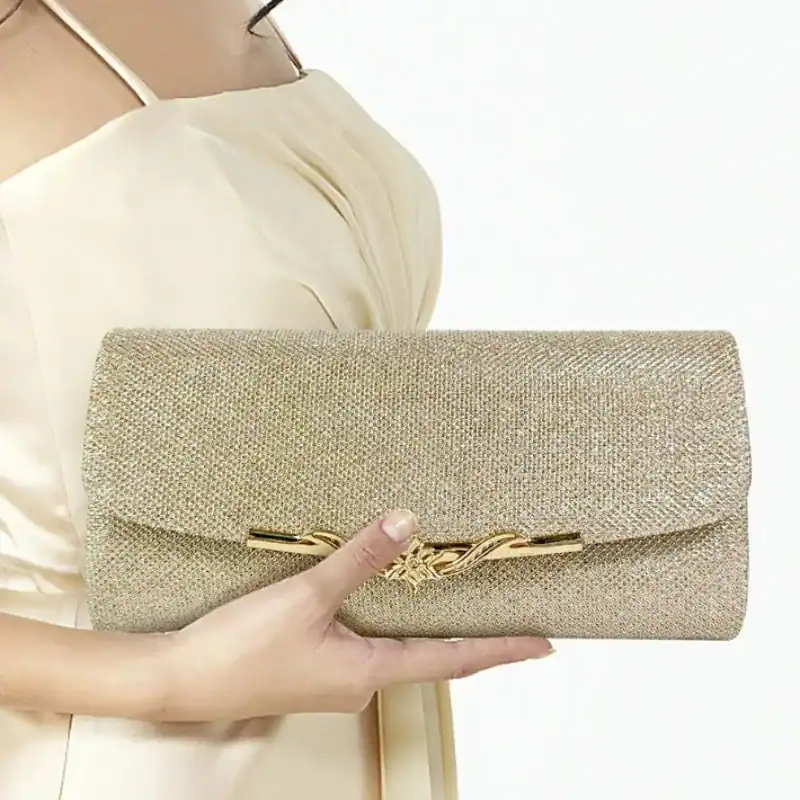 Beige vävd clutch med guldaktig metallisk snabb, hålls i handen av en kvinna.