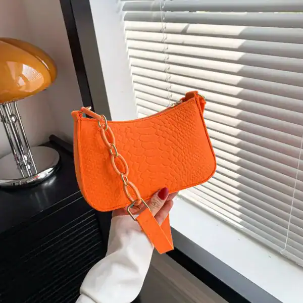 Blå axelremsväska i orange, med krokodilmönster och kedjehandtag.