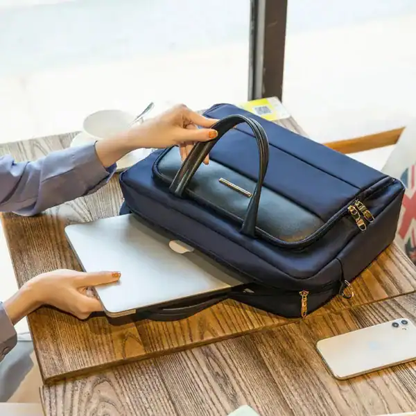 Blå datorväska med handtag, öppen för att visa innehåll, på träbord med laptop och mobil.