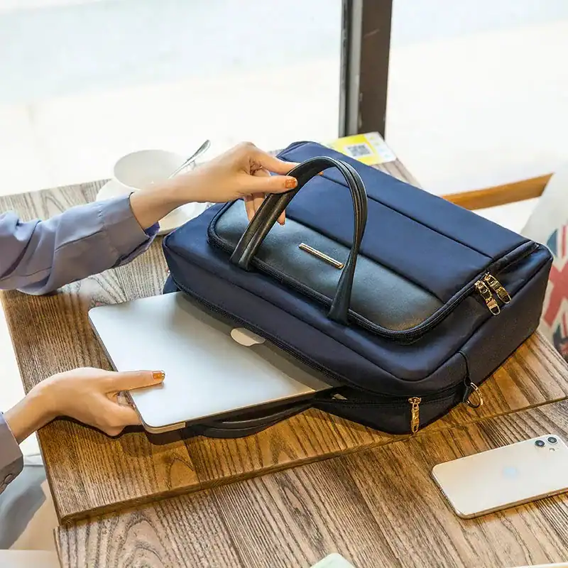 Blå datorväska med handtag, öppen för att visa innehåll, på träbord med laptop och mobil.