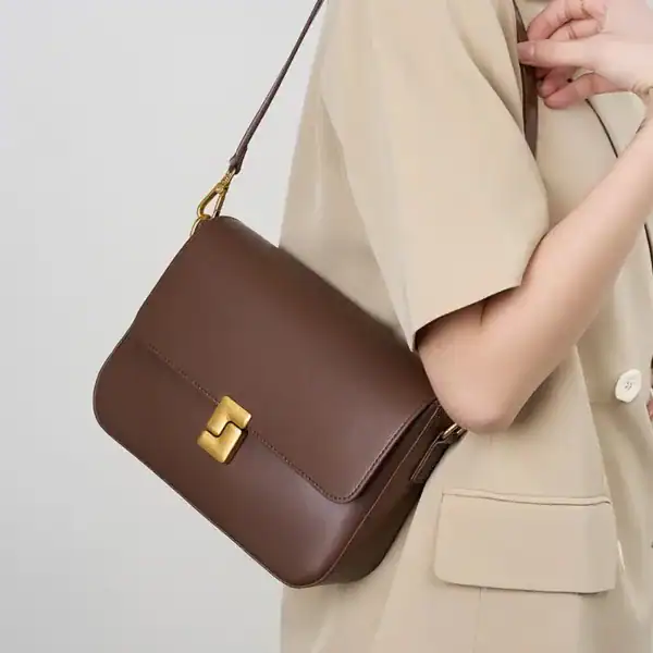 Brun axelväska med guldlock, bärs över axeln av kvinna i beige kläder.