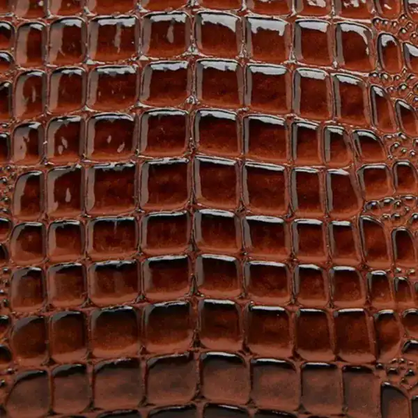 Brun krokodilmönstrad väskmaterial, texturerad yta med glansig finish.