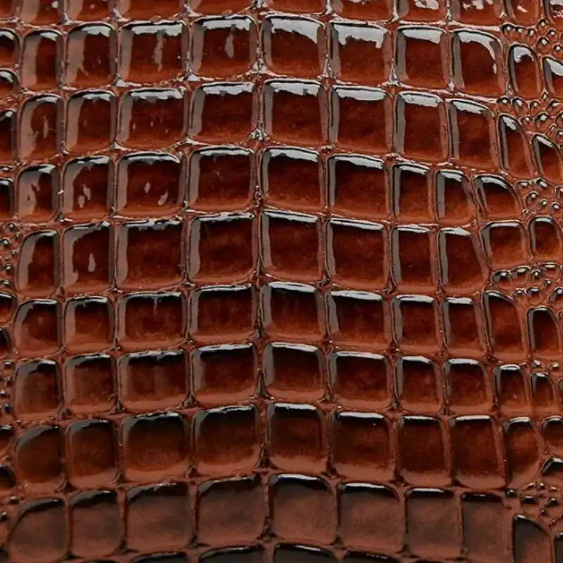 Brun krokodilmönstrad väskmaterial, texturerad yta med glansig finish.
