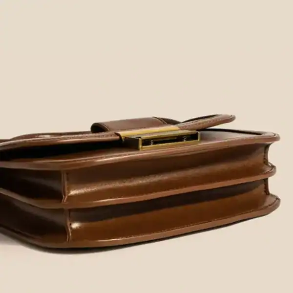 Brun liten axelremsväska med metallficklås och elegant design.