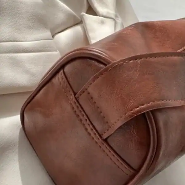 Brun liten axelväska i läder med detaljerad sömn och elegant design.