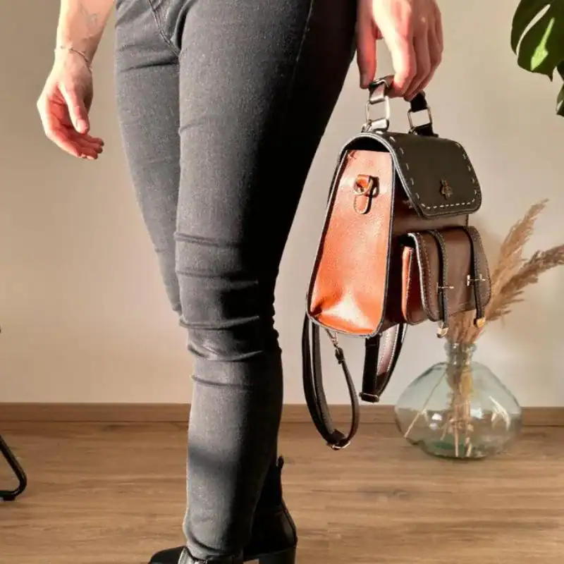 Brun liten ryggsäck i läder, hållen i handen av en person i jeans.