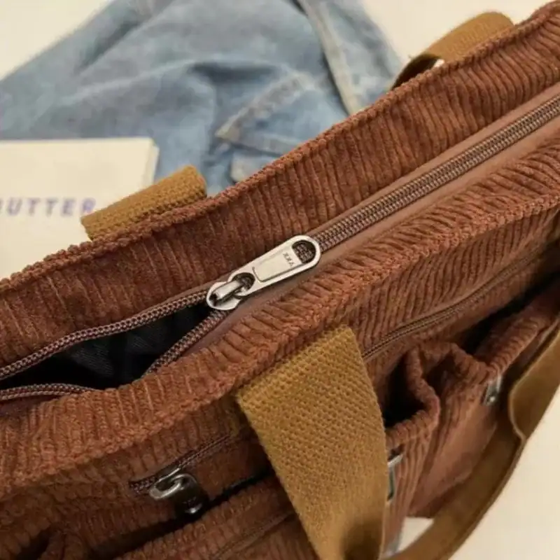 Brun manchester hinkväska med dragkedja och textilhandtag.
