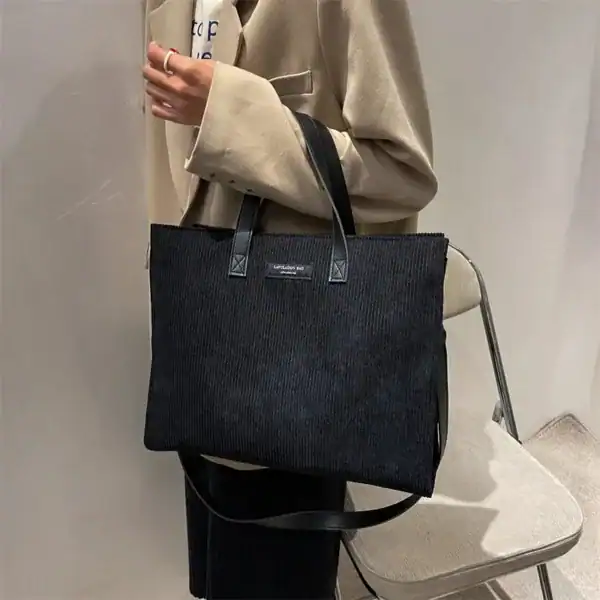 Brun Manchester shoppingväska med strukturerad textil och svarta handtag.