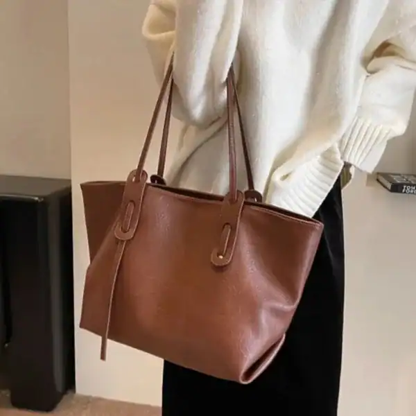 Brun shoppingväska i läderliknande material, modell med axelrem och handtag.