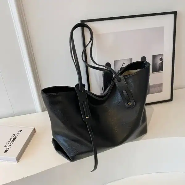 Brun shoppingväska i svart läder, stor handväska med axelrem och dragkedja.