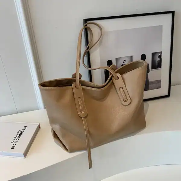 Brun shoppingväska i läderliknande material med långt handtag och minimalistisk design.