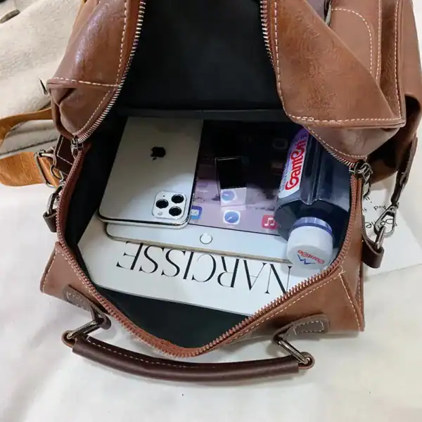 Brun skolväska med spännen, fylld med mobil, tablet och dryck.