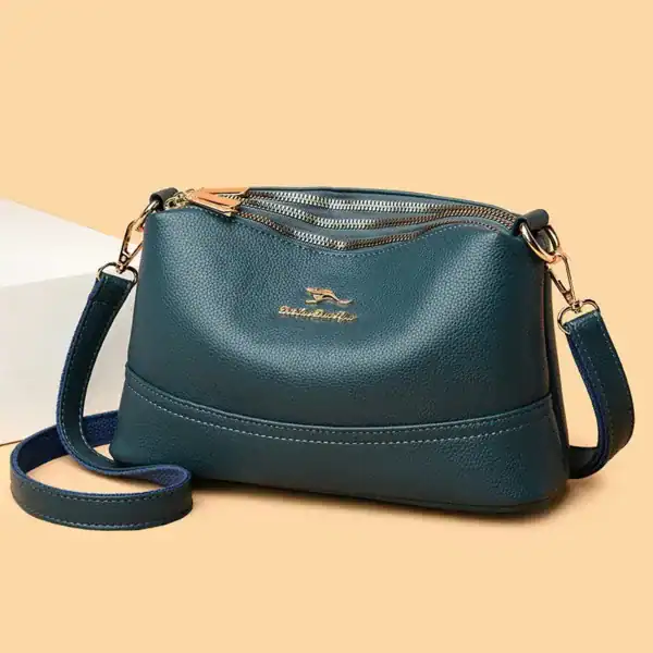 Cognac liten crossbody axelväska i mörkblått läder med guldtonade dragkedjor och axelrem.